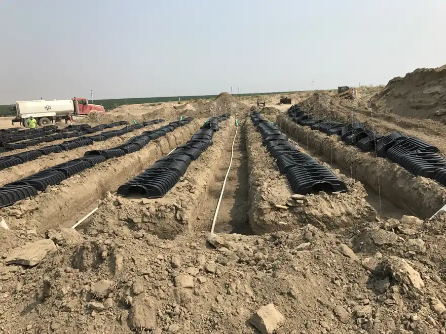 Long rows of black infiltrator chambers laid in open trenches across a large flat commercial site