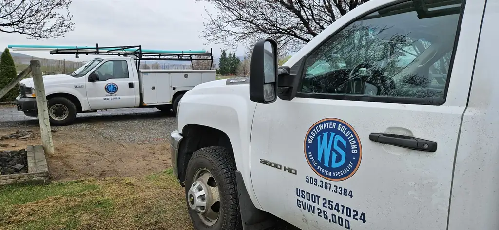 Two white Washington Wastewater Solutions service trucks parked side by side, the navy and orange roundel on each door