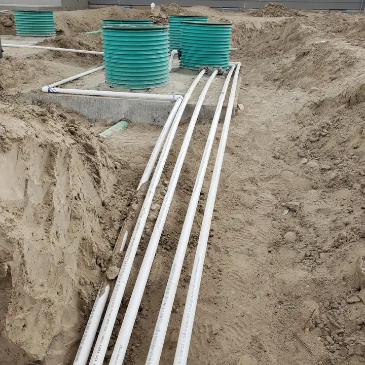 Three green access risers and white supply pipes set into a fresh excavation