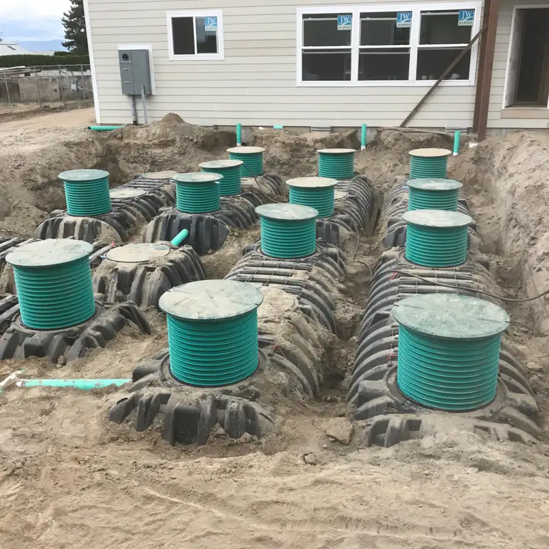 Green riser lids and rows of chambers set in fresh soil beside a house, ready for inspection before backfill