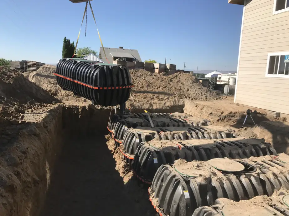 A black poly septic tank swinging on a crane line over a trench of infiltrator chambers