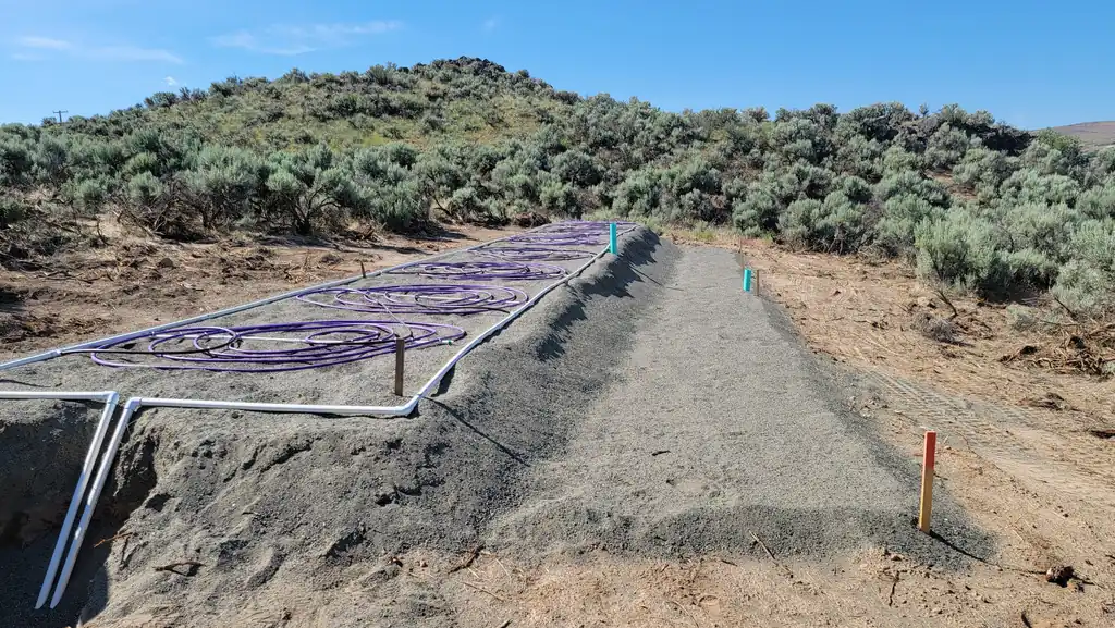 A graded drainfield bed on a hillside with white pressure laterals and grade stakes