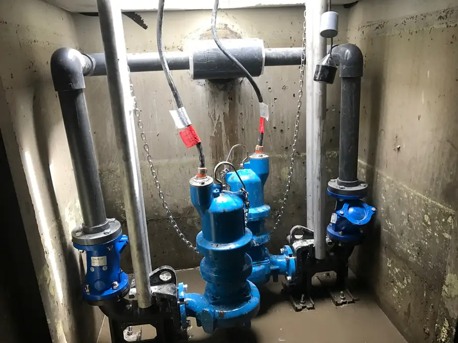 Two blue septic pumps and grey PVC plumbing inside a concrete pump vault on a commercial job