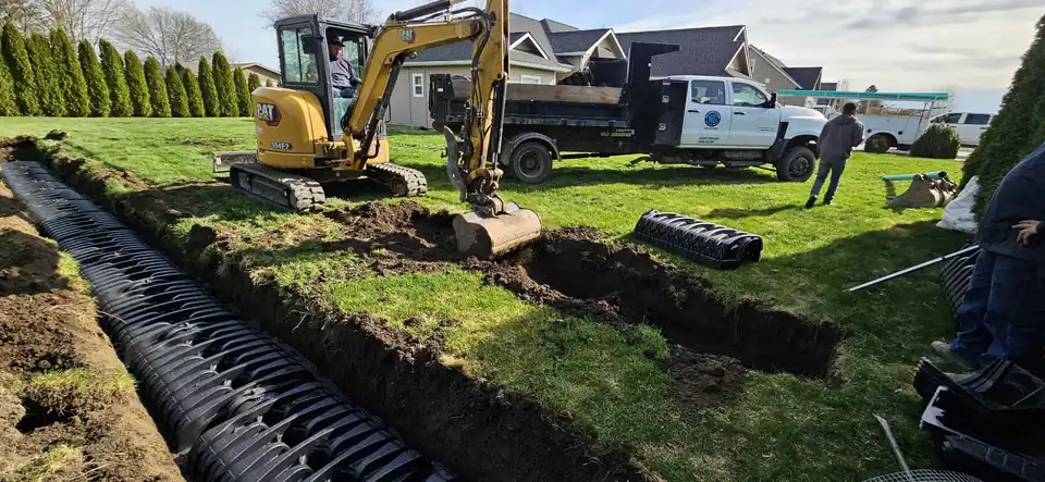 A Wastewater Solutions crew cutting a trench across a green lawn with a mini excavator, chambers laid in the trench and the company pickup behind